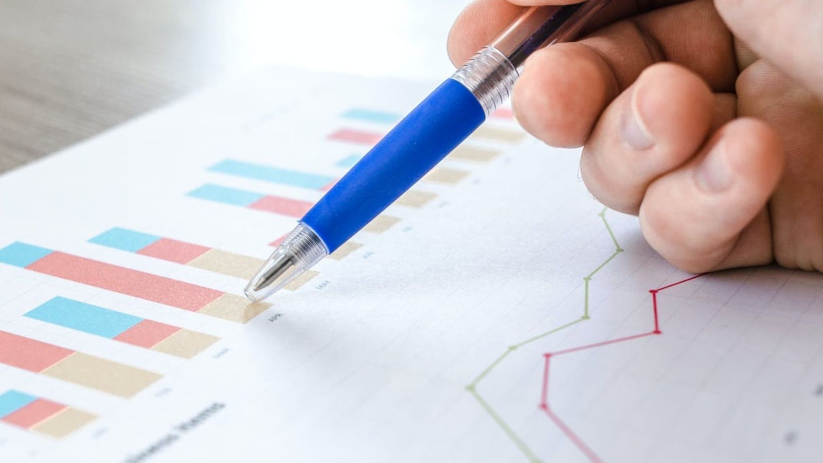 Close up of a hand holding a pen, pointing at a page with graphs.