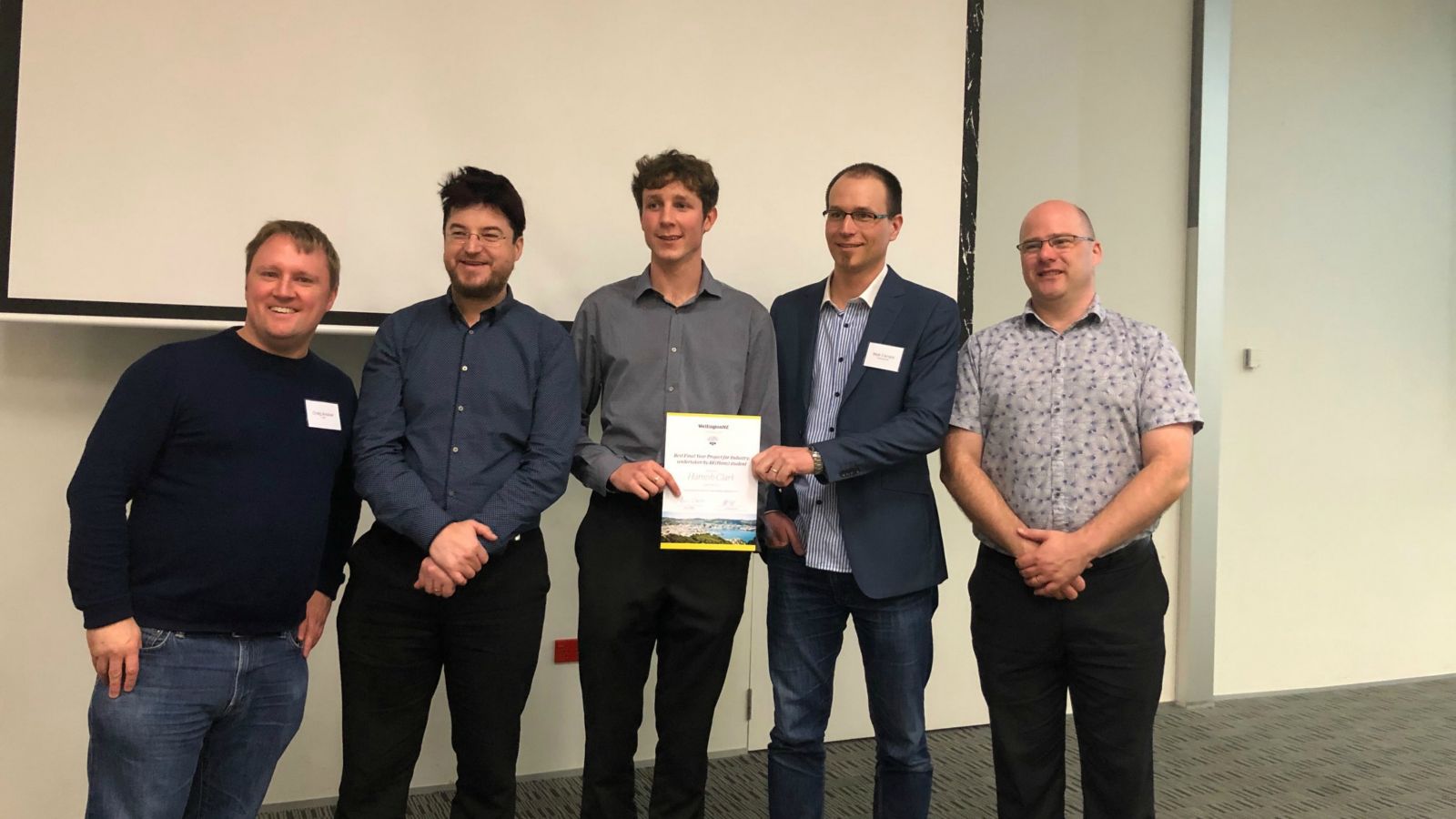 A group of five men stand with a certificate: Hamish Clark, centre, with SECS and WellingtonNZ staff after being presented with the Best Industry Project award.
