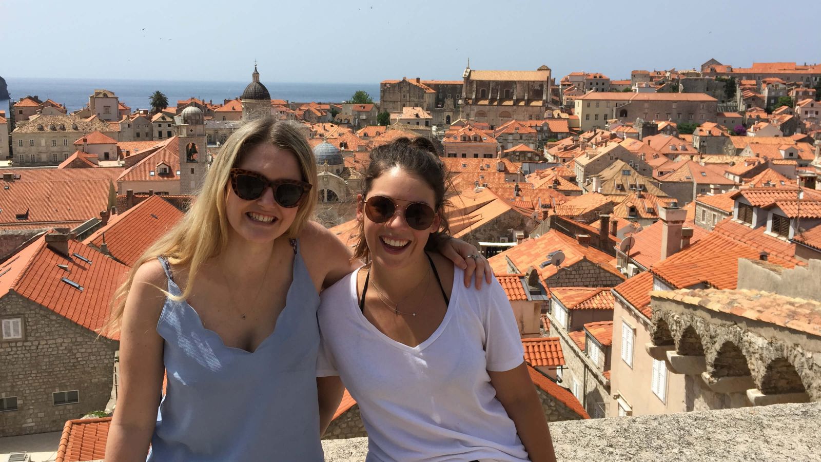 Two students smiling and standing side by side on a sunny day with a view of Dubrovnik, Croatia behind them.