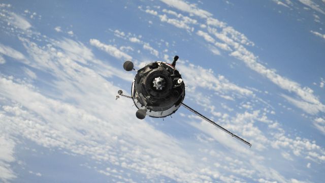 A satellite flying in front of clouds and blue sky.