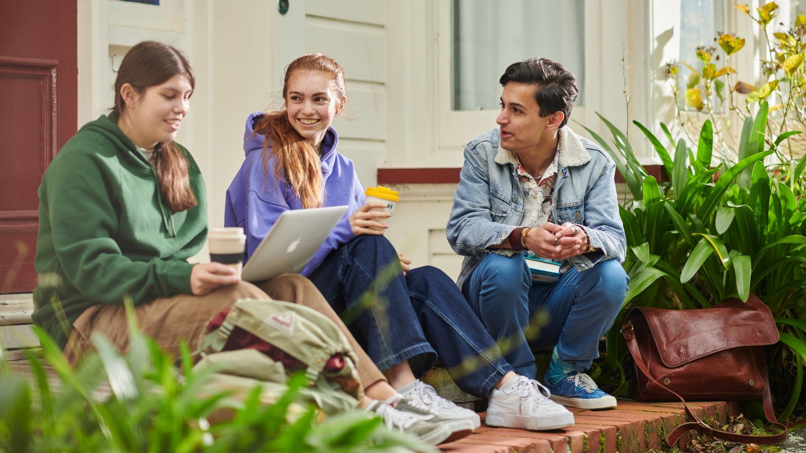 Three students sitting on the steps outside their hall of residence.