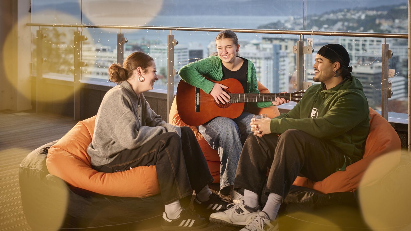 Three residents sitting on beanbags on a balcony at a hall of residence, with a guitar