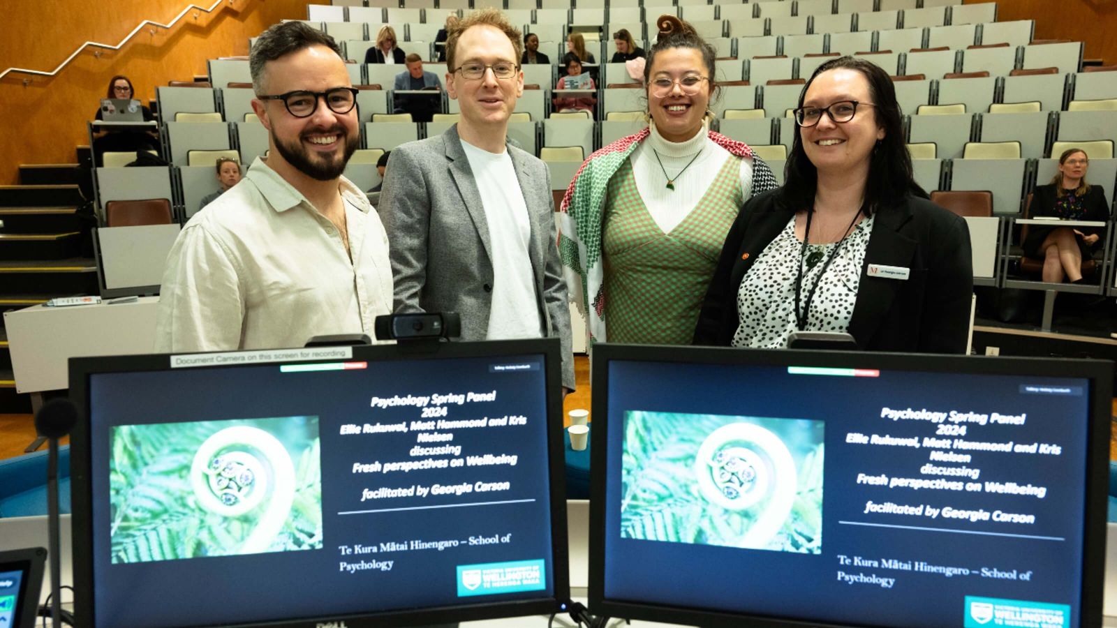 Four academics, standing behind two computer screens reading Psychology Spring Panel