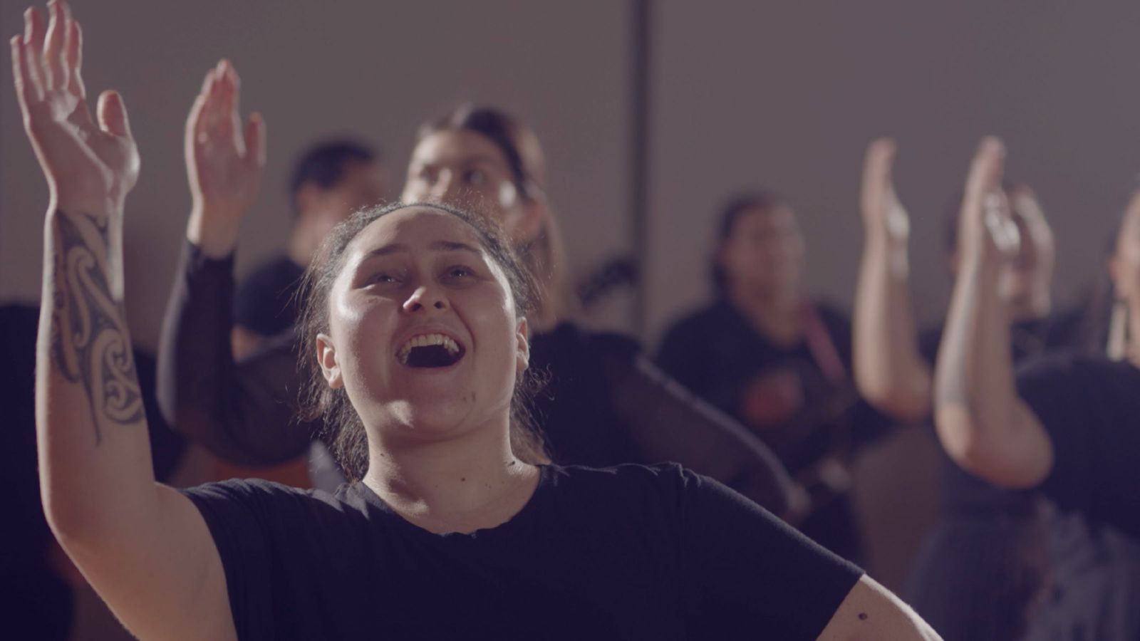 A close up of a woman with her head held high and one hand pointing upwards as she sings.