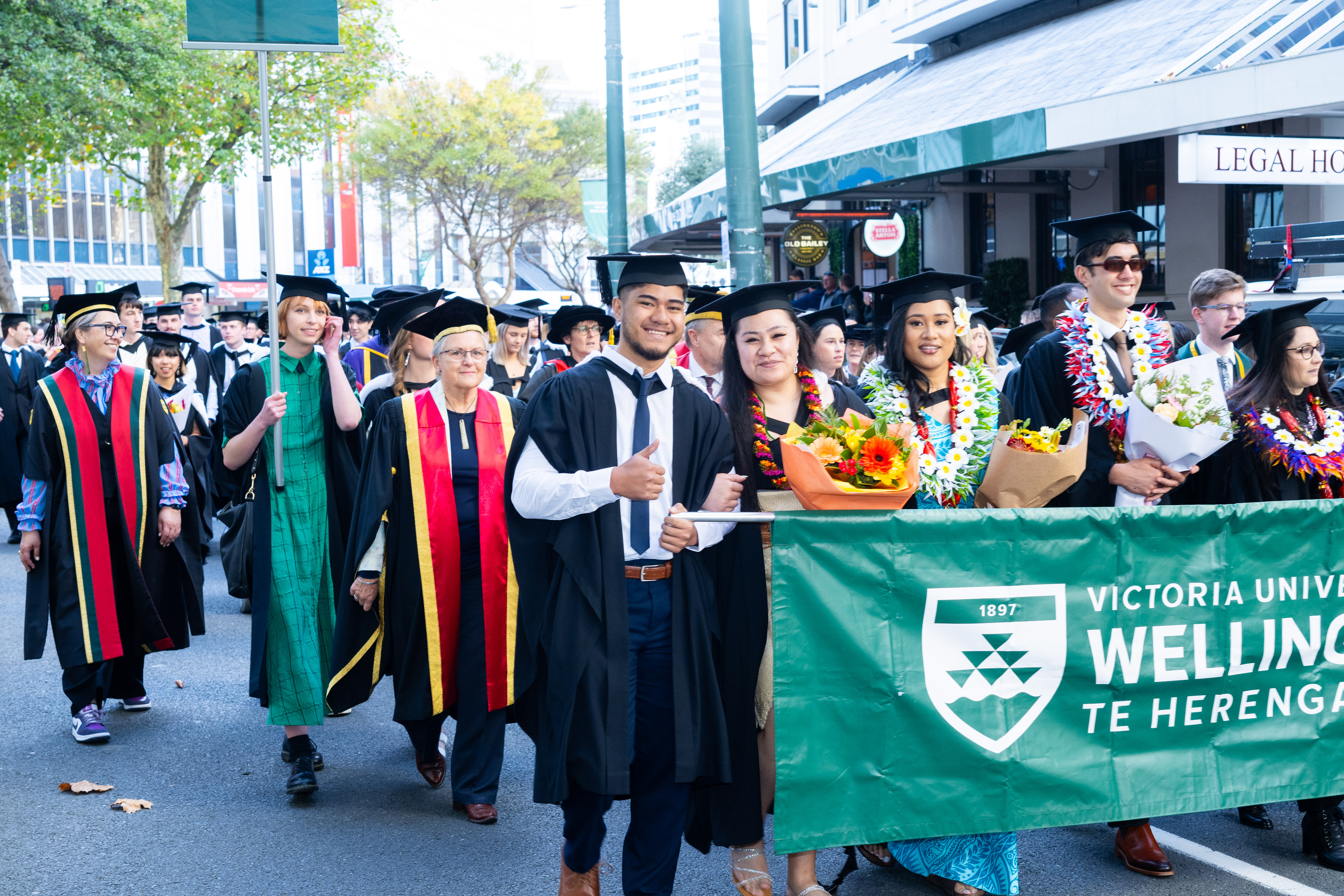 A picture of students in academic dress holding flags and a banner in a graduation parade in central Wellington. 