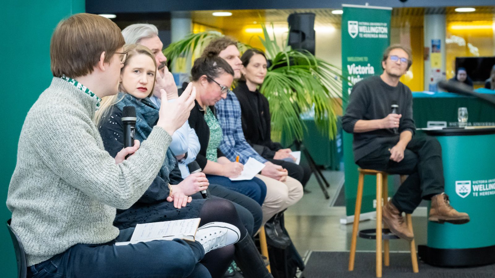 A group of academics seated on stools in a row, engaged in a panel discussion.