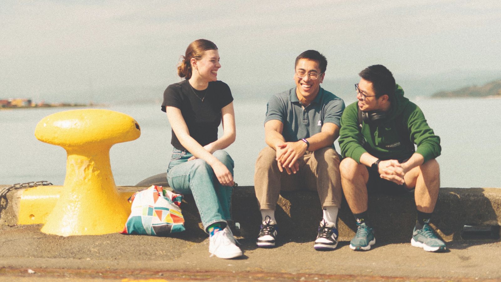 Three students sitting on the Wellington waterfront, next to a big yellow metal object