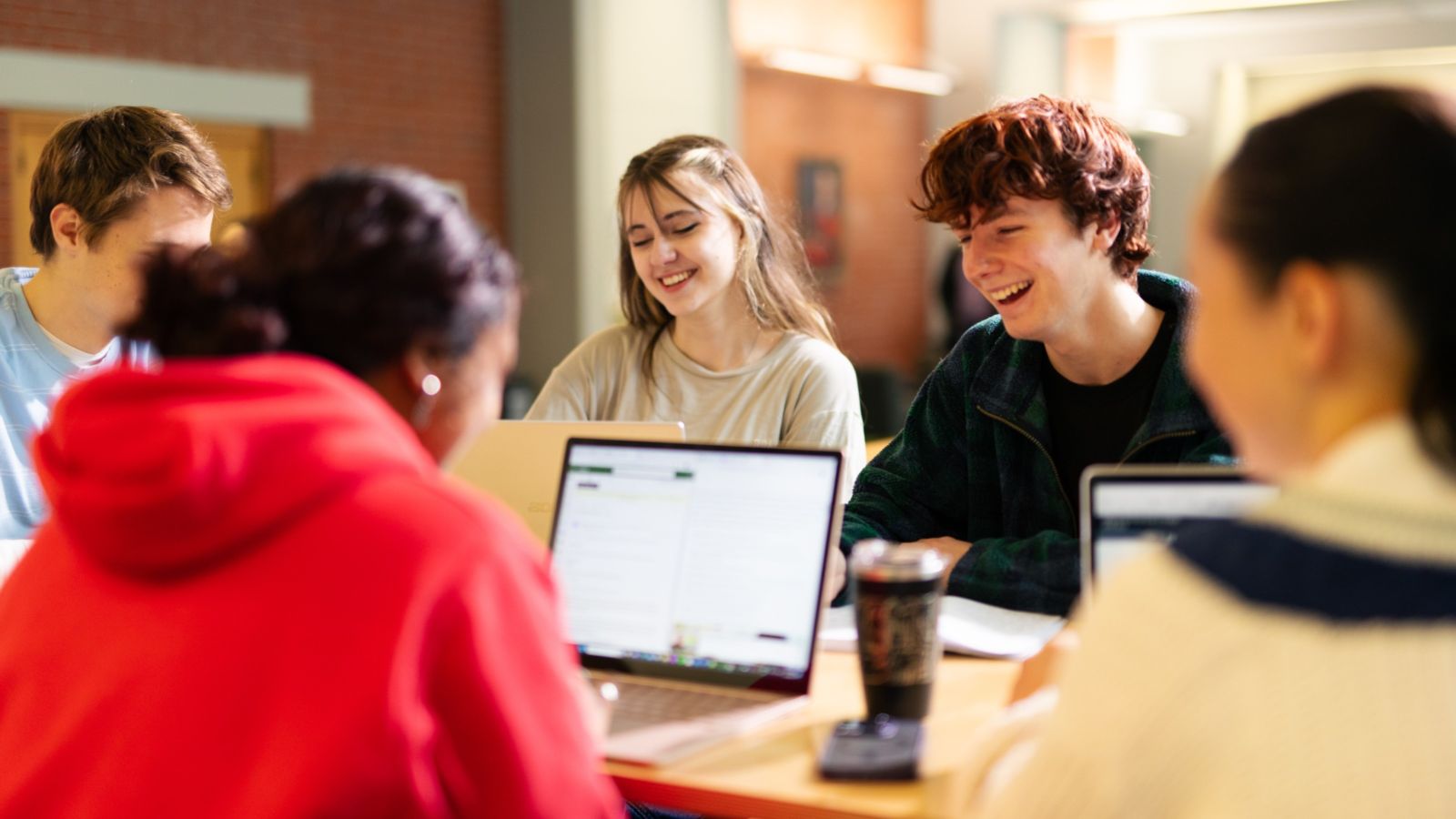 A mix gender group of smiling students sitting around a table with their laptops 