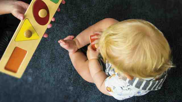 Adult holds wooden shapes puzzle for child to see and play with.