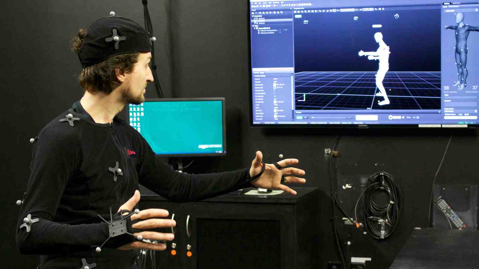 A student wears a motion capture body suit and looks at his avatar on a monitor.