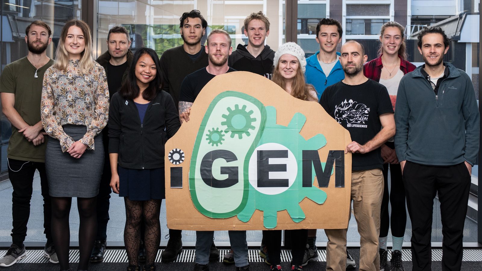 Team of young people stand behind iGEM logo.