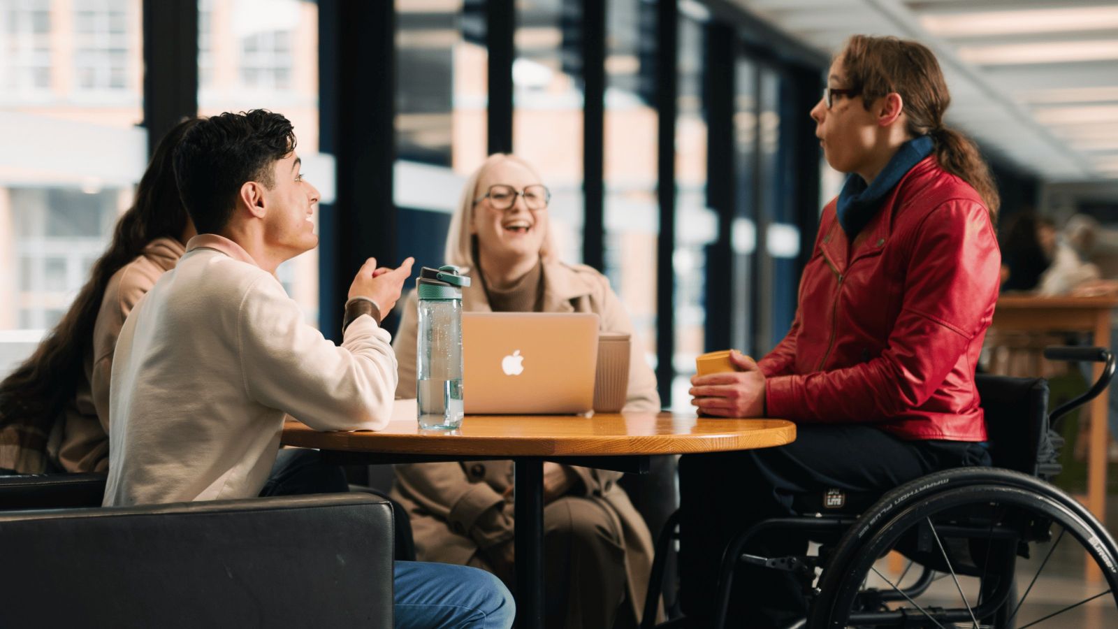 A photo showing four students sitting around a table talking, one is in the wheelchair.