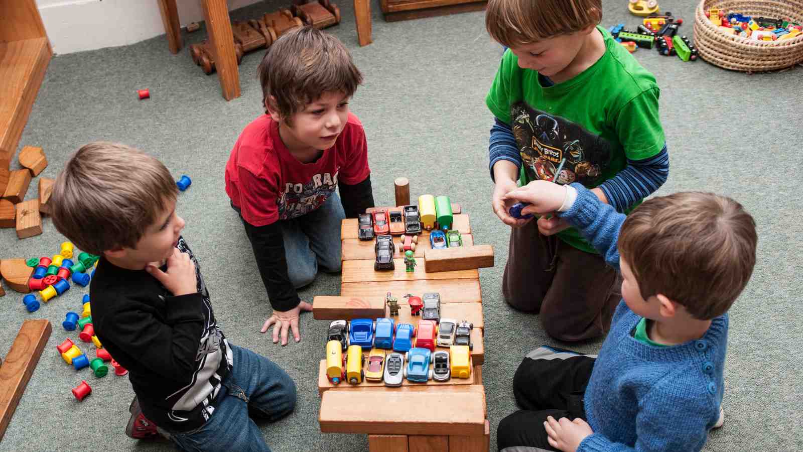 Four young boys play with blocks and toy cars together. 