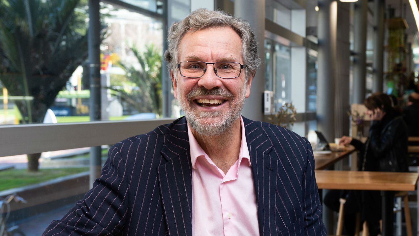 Professor Arthur Grimes smiles in blue suit and pink shirt.