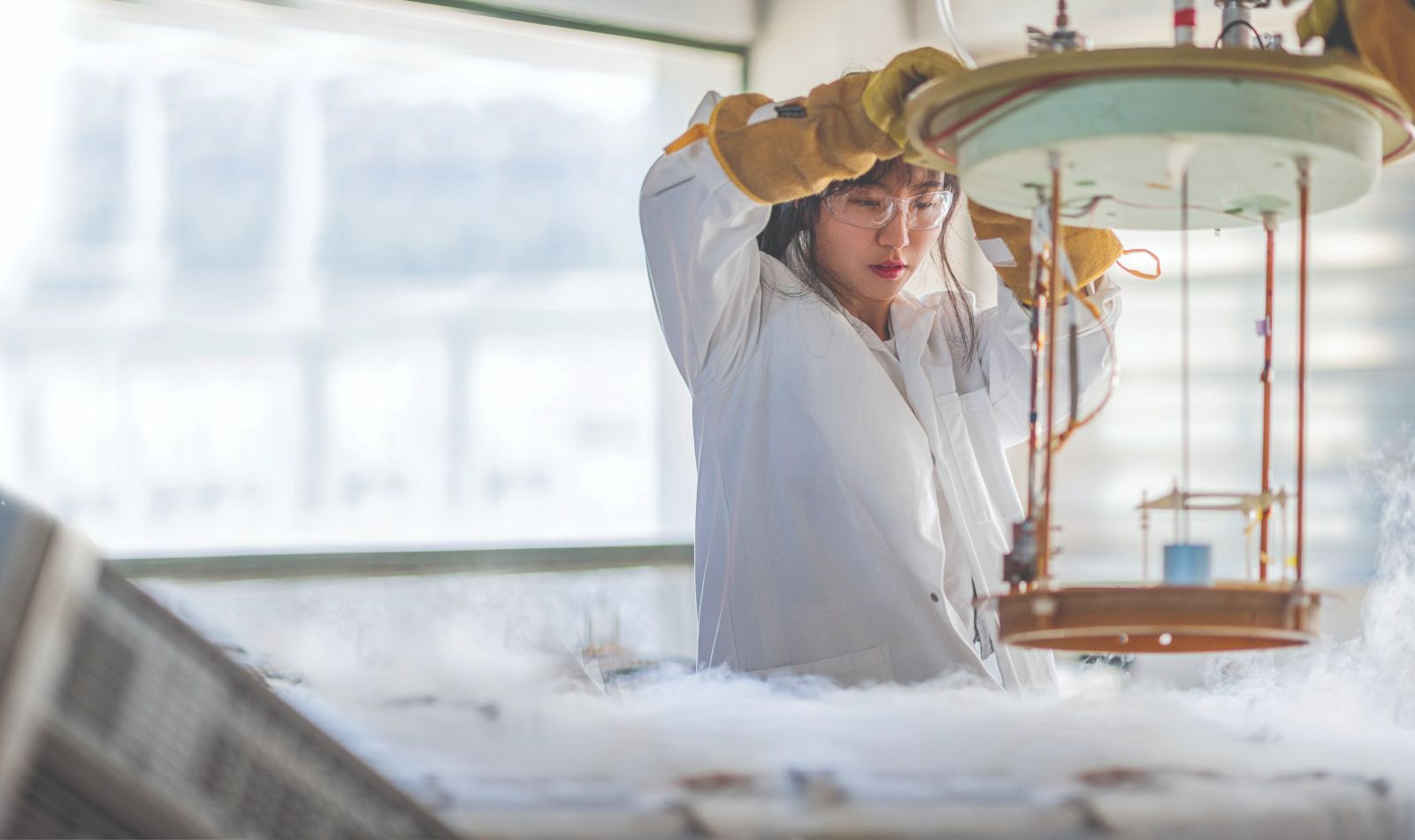 A female student, using a large piece of scientific equipment with vapour rising out of it. Image copyright Victoria University of Wellington.