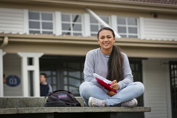 Female student sitting outside house with study books