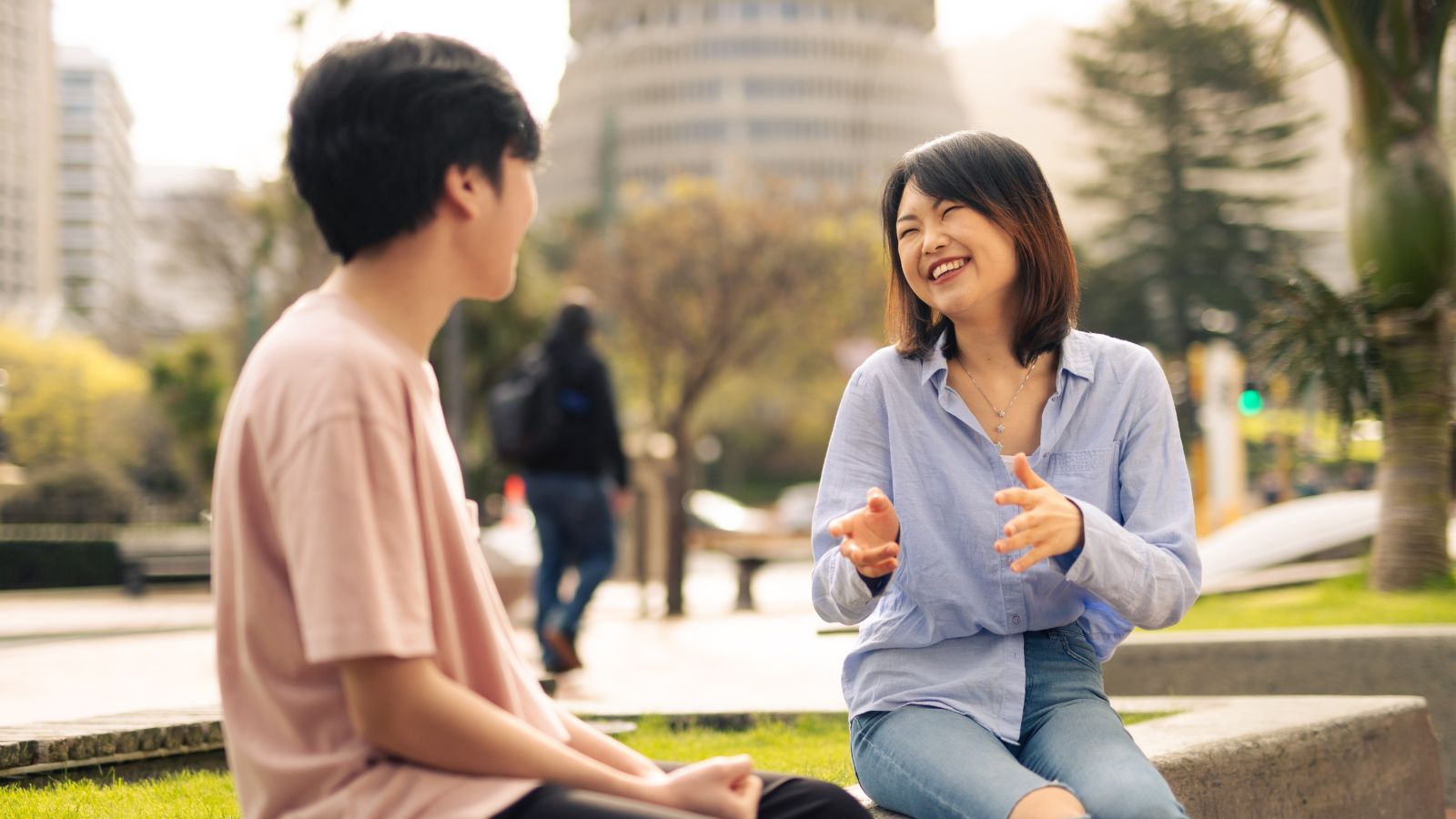 A photo showing two young people sitting on the grass and smiling with the beehive in the background. 