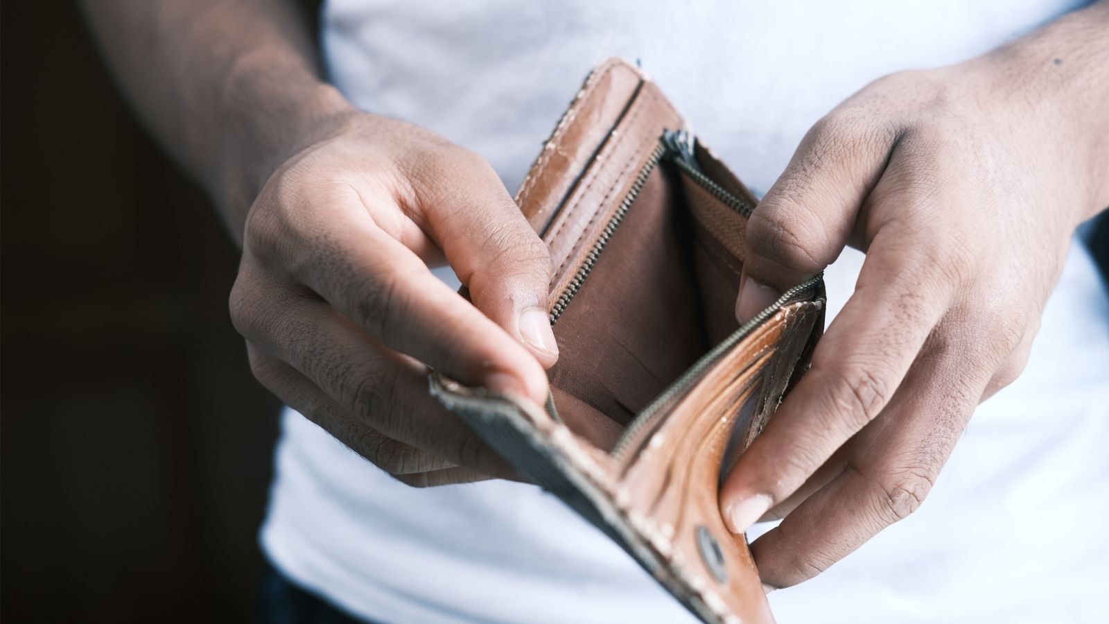 A close up of a man's hands holding open a leather wallet to show that it is empty.