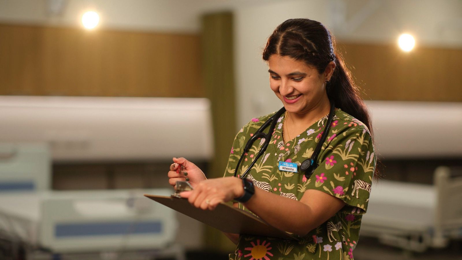 A nurse in colourful scrubs consults a clipboard of notes.