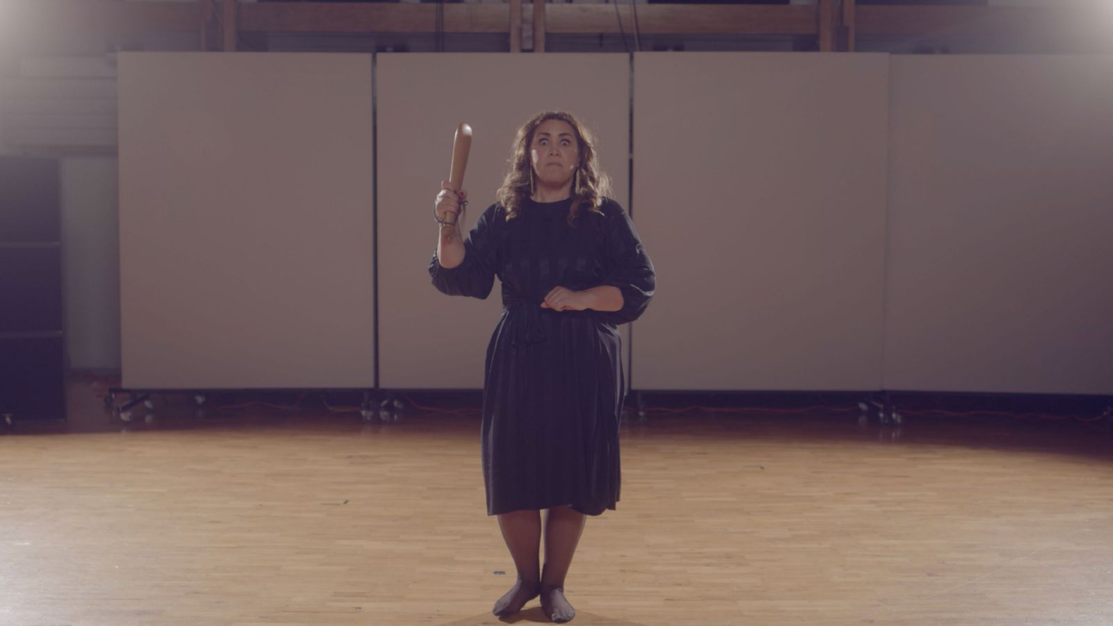 A woman holding a wooden club staring fiercely ahead.