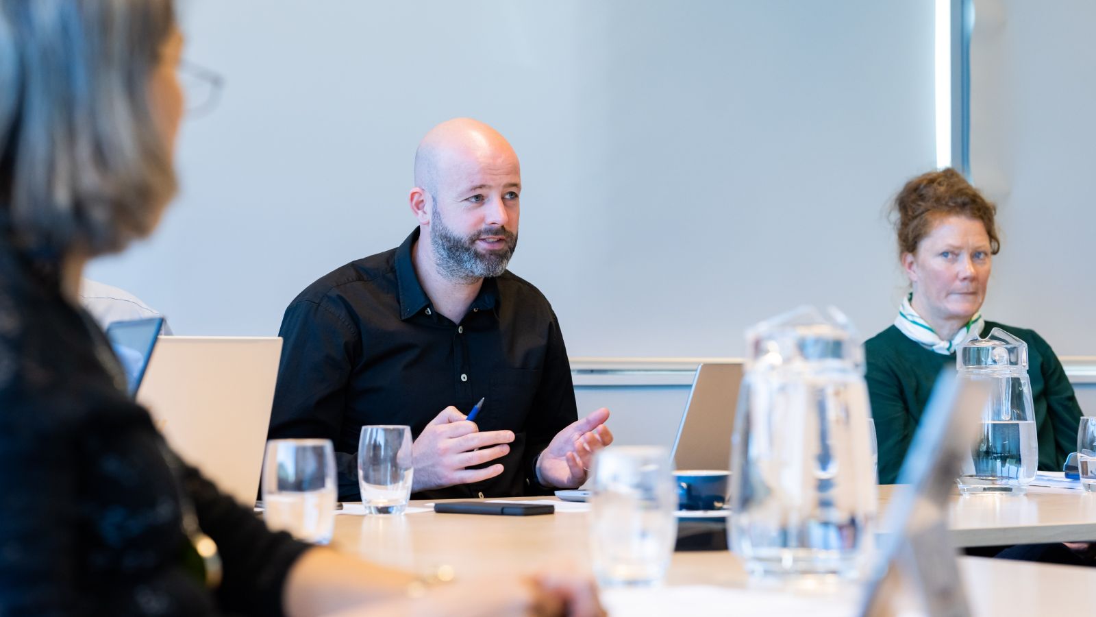 Three academics sat at a table discussing, two are in focus, and one is out of focus in the foreground.