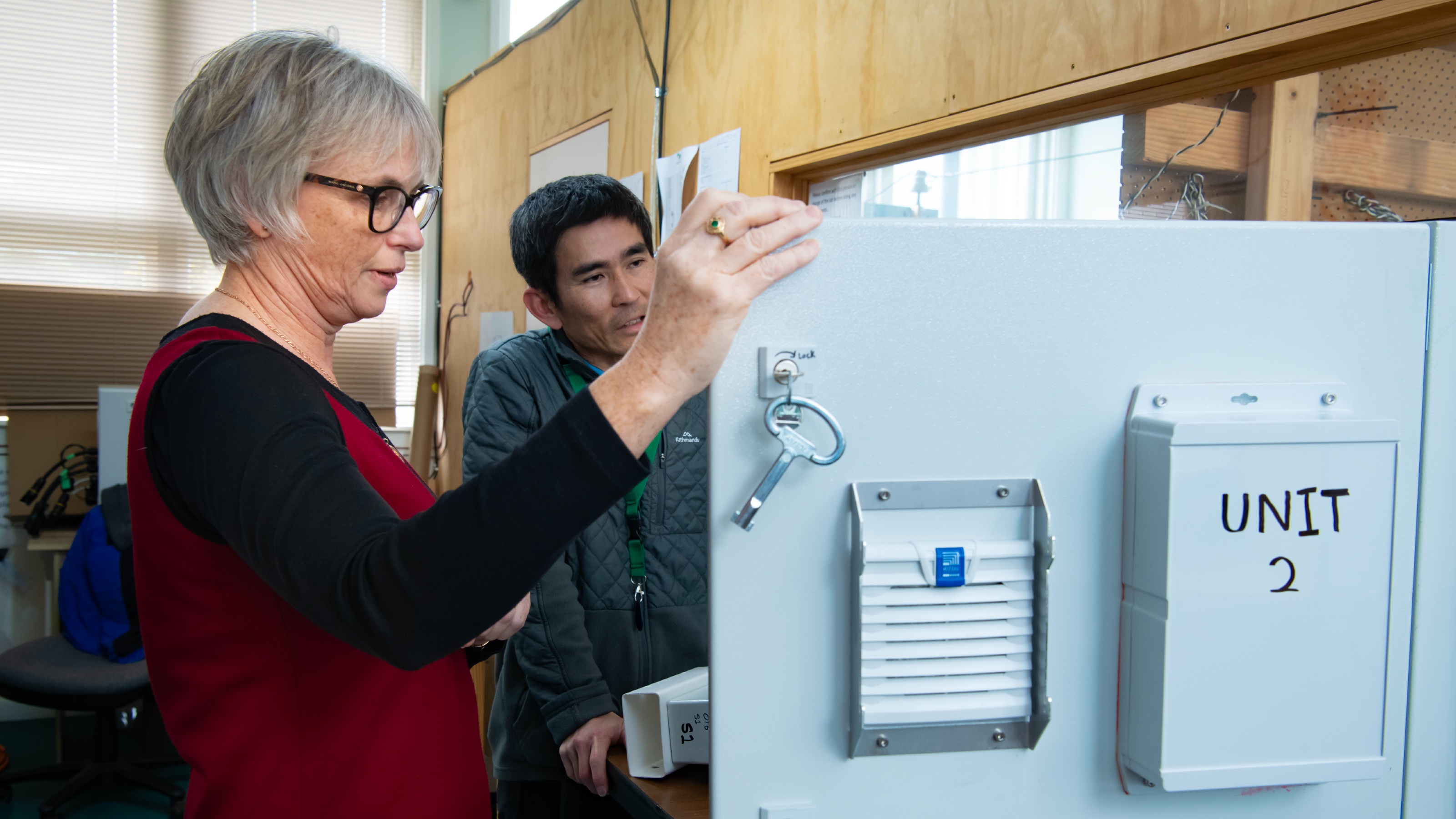 Two researchers look over and discuss a piece of scientific equipment labelled Unit 2