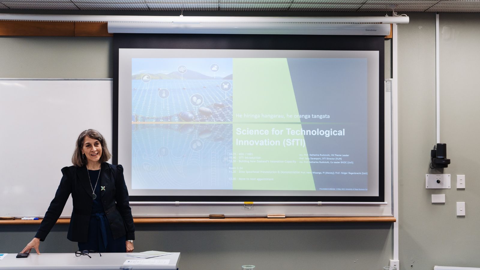 AProf Katharina Ruckstuhl stands to the left of a projector screen at the front of a room