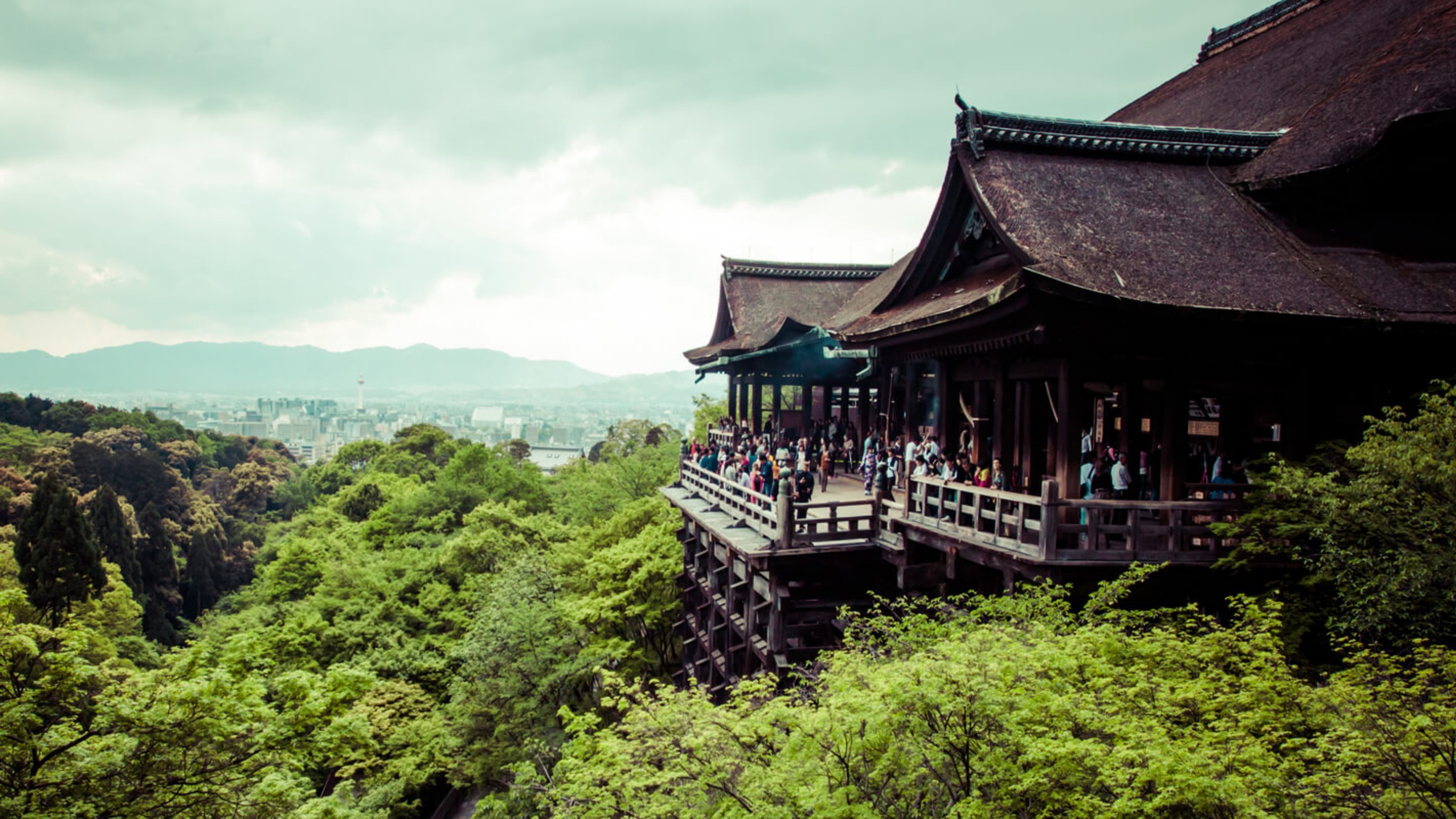 View of ancient wooden temple with forest in foreground and city in background