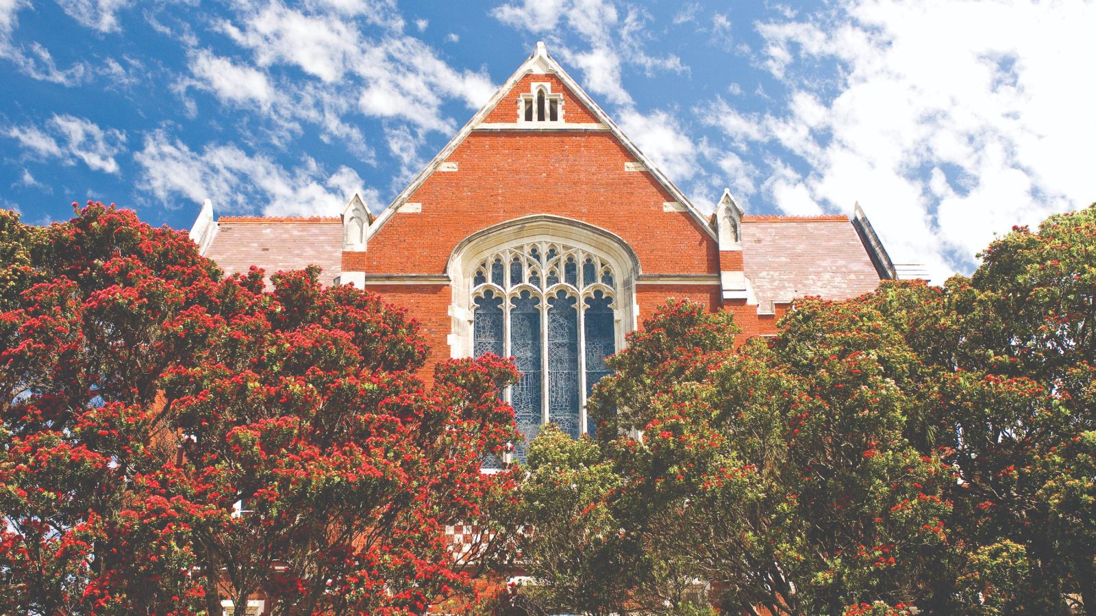 Large brick building with blue sky behind and tall trees in front 