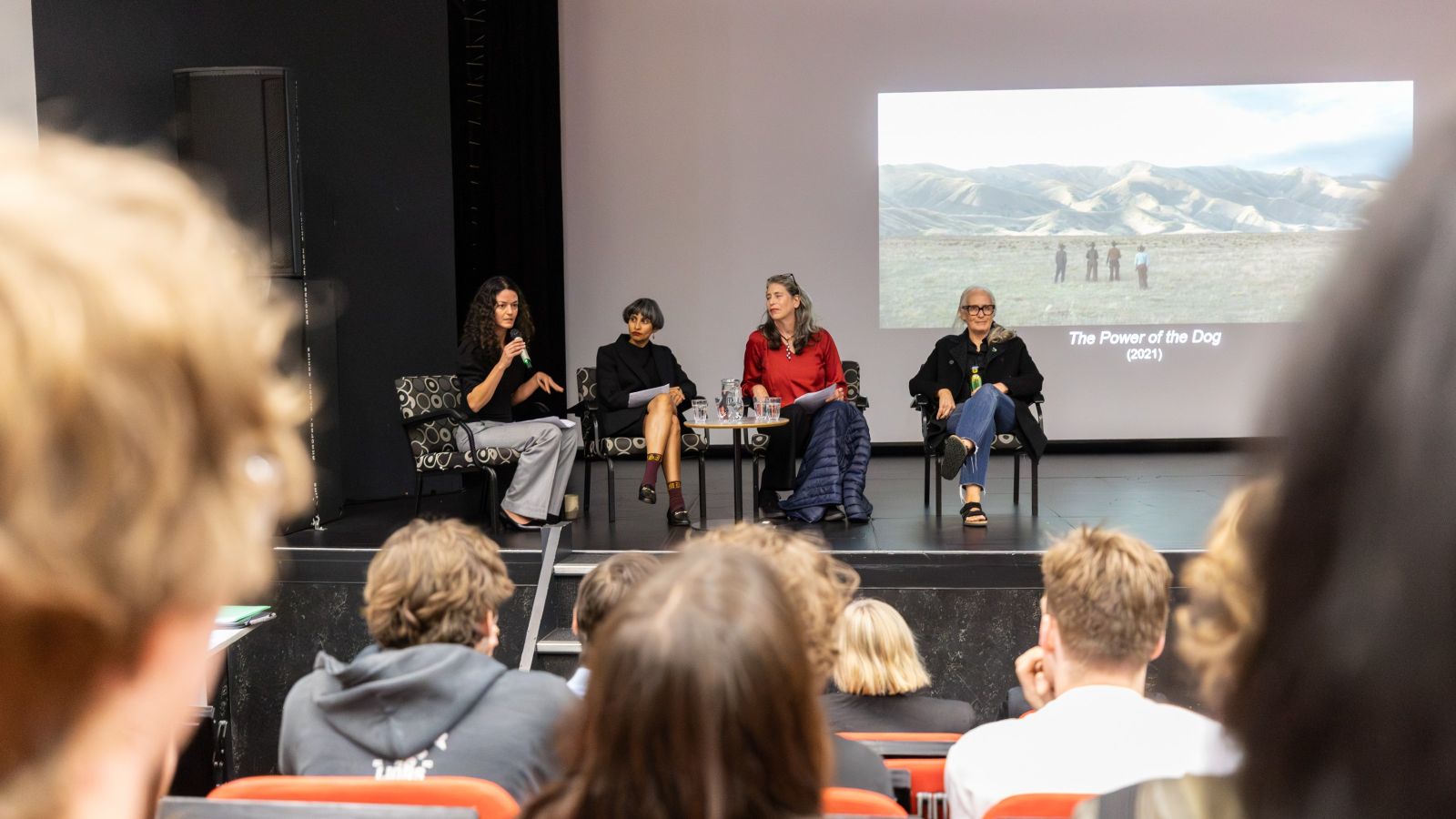 Jane Campion sits on stage next to three Victoria University lecturers. The photo is taken from behind students sitting in the audience.