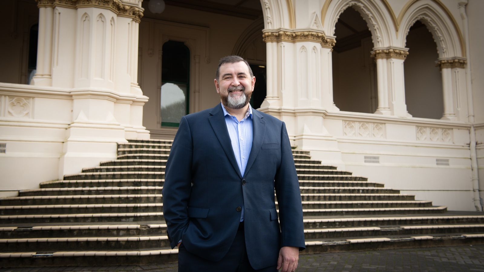 David Wilson standing in front of parliament steps, wearing a suit and smiling at the camera.