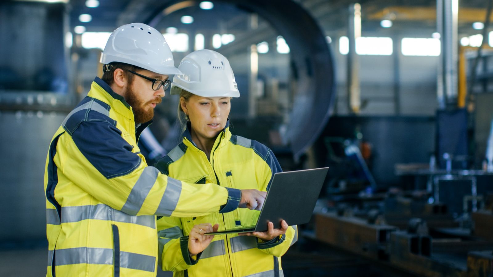 Two people in hard hats and high vis jackets looking at a laptop together