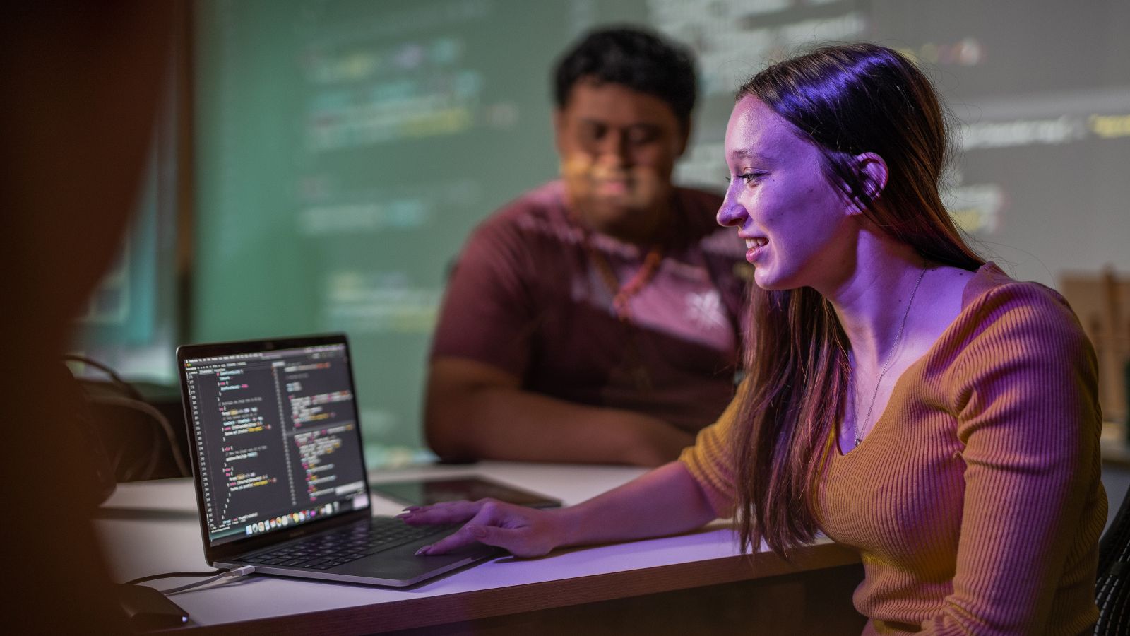 A student sits in front of her laptop with computer code on the screen. The code is being projected on to the walls as well