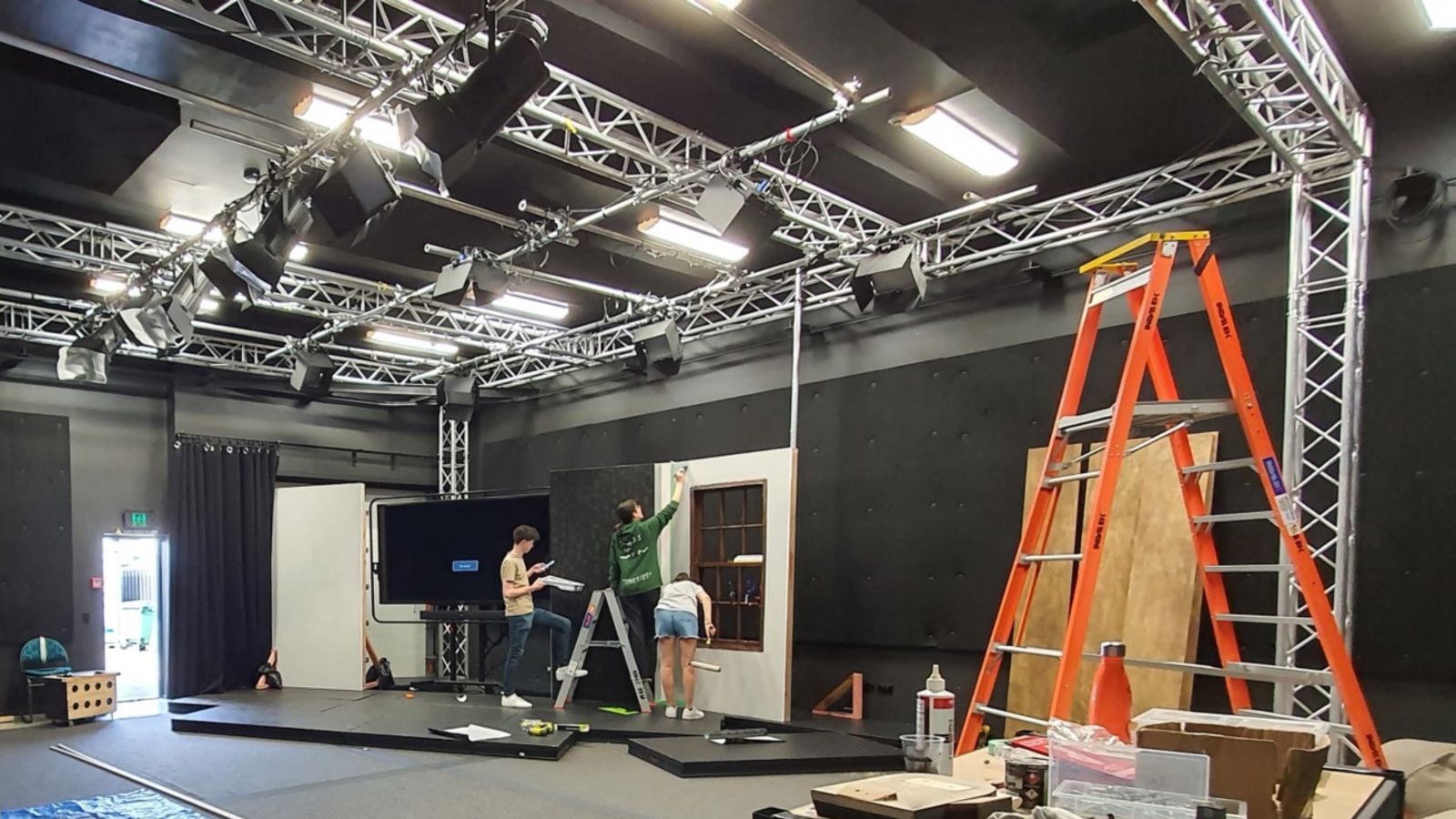 3 people paint and work on a set build in a large studio