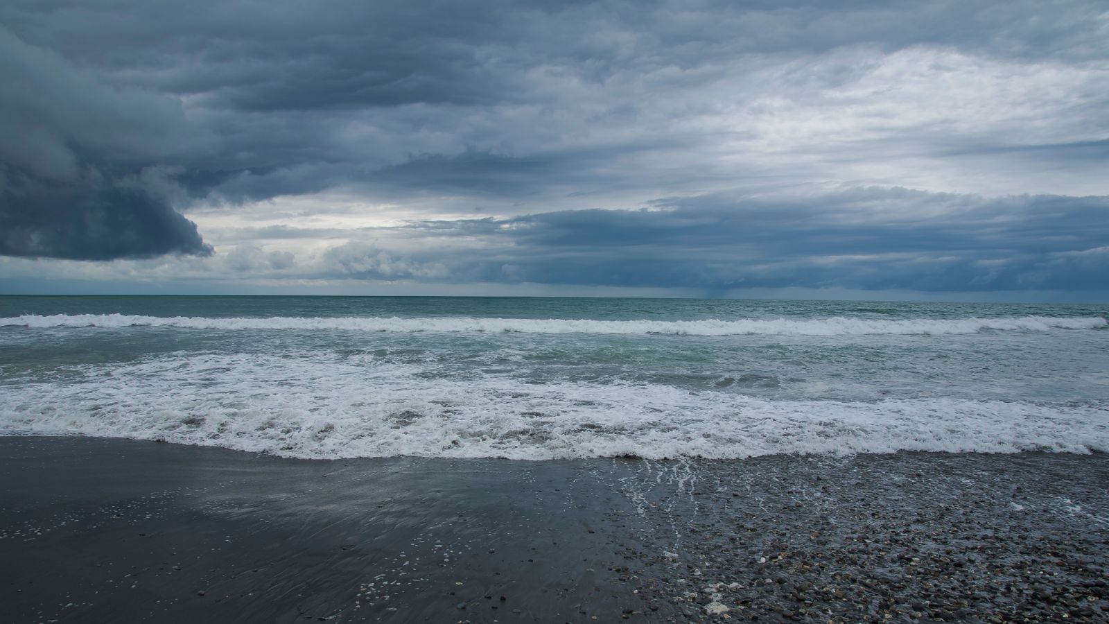 Waves on a sandy beach with cloudy sky above 