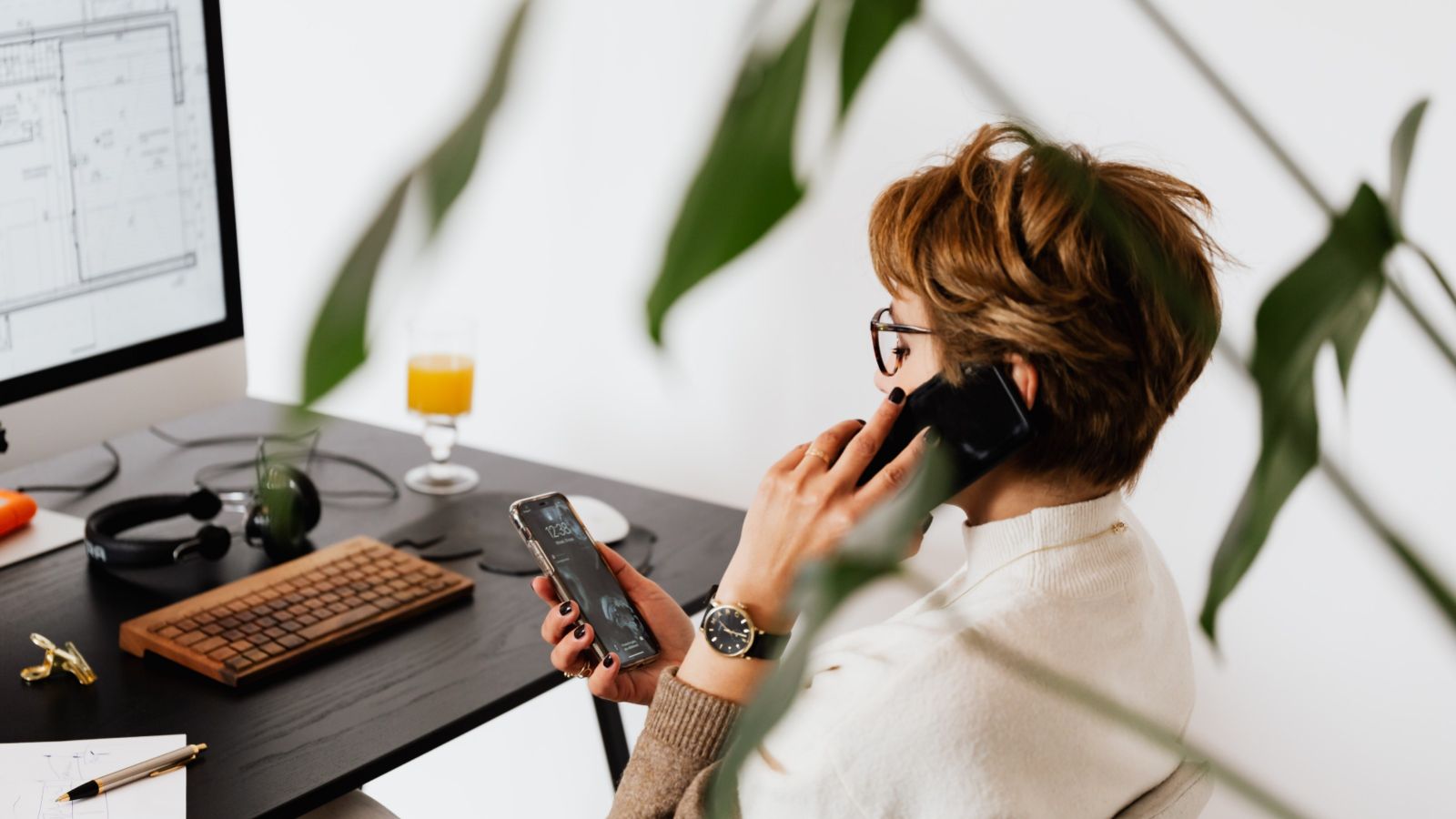 Woman at desk, talking on a phone and checking messages