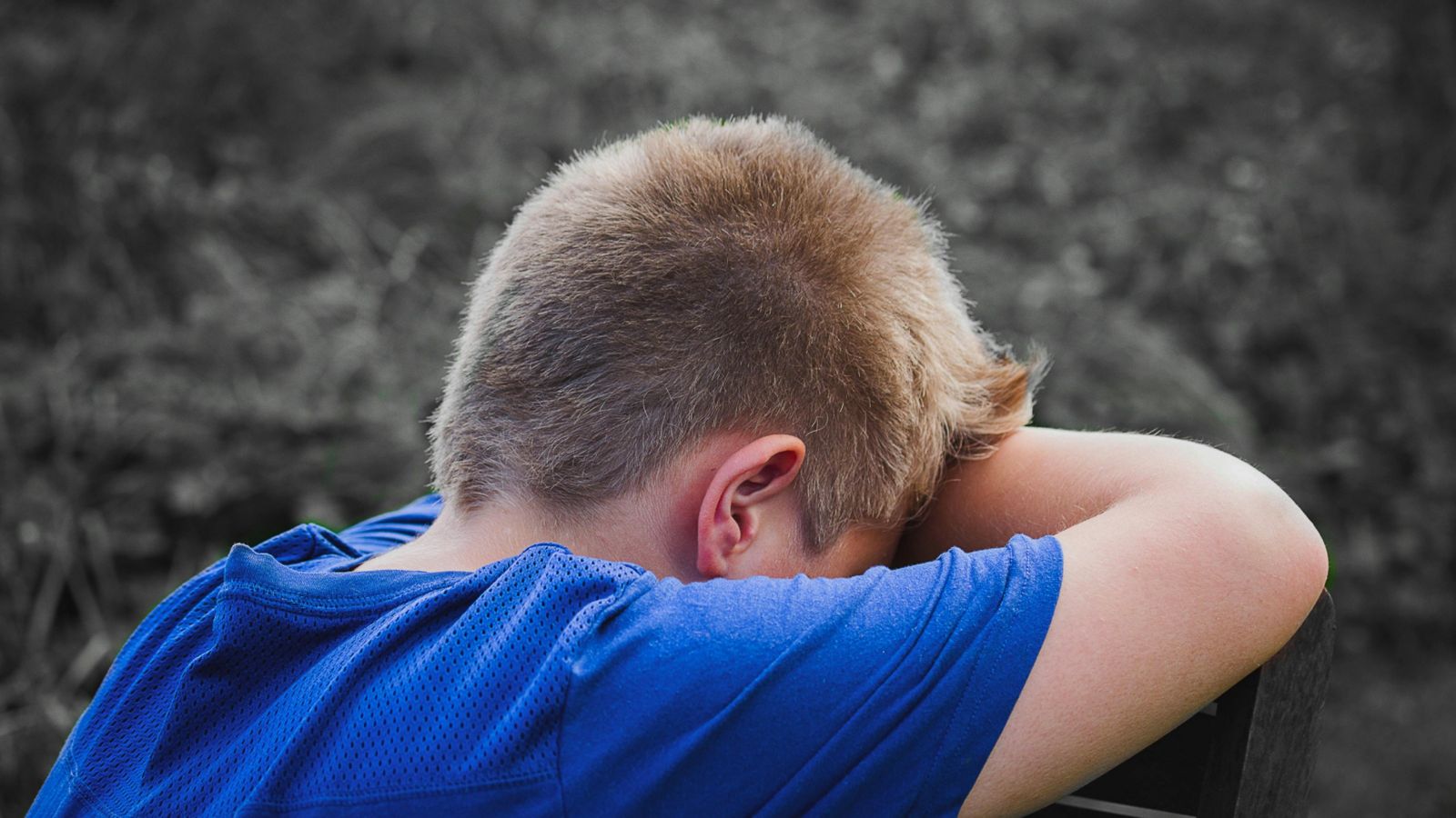 Child with head in hands leaning on wooden seat 