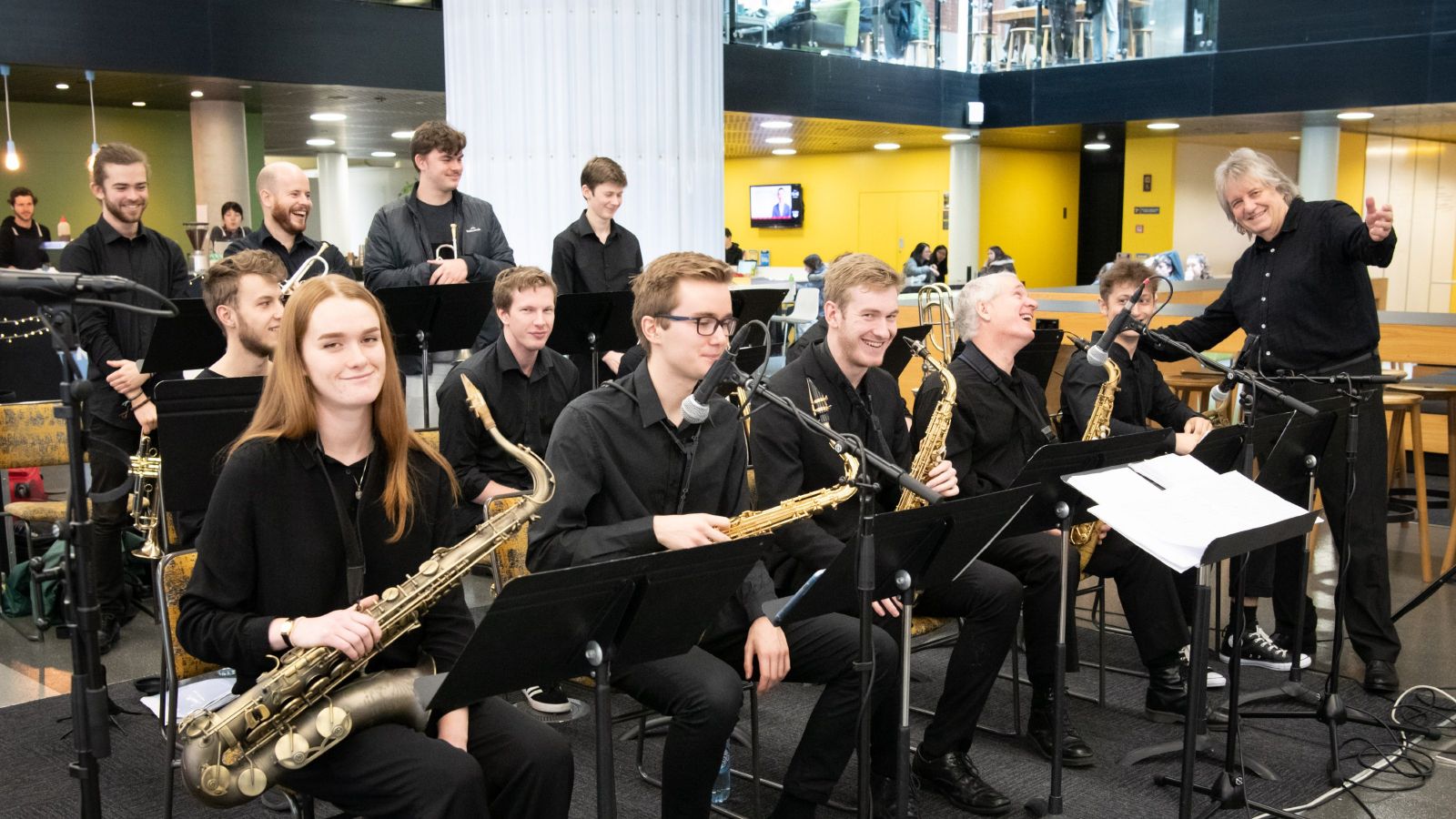 Rodger Fox is smiling and standing with some students who are seated and holding their instruments.