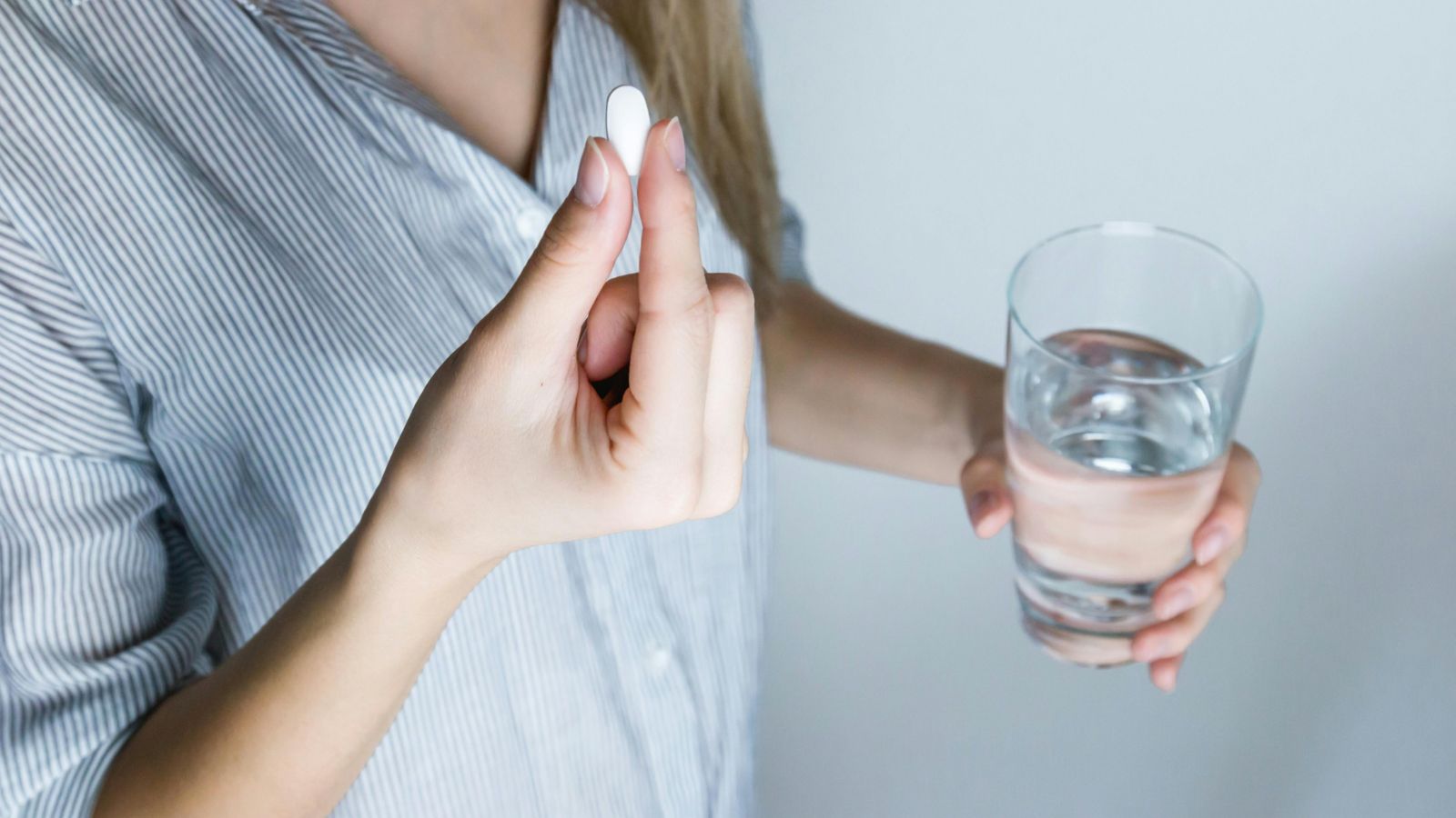 Person holding a pill and glass of water 