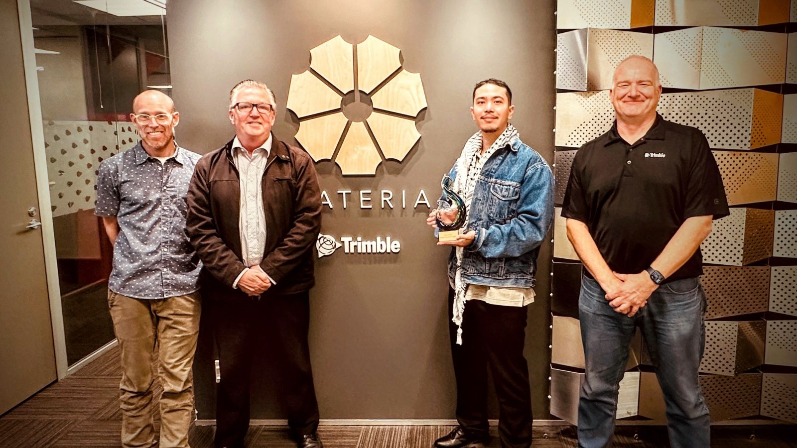 Four men posing for camera in front of office, one receiving gift