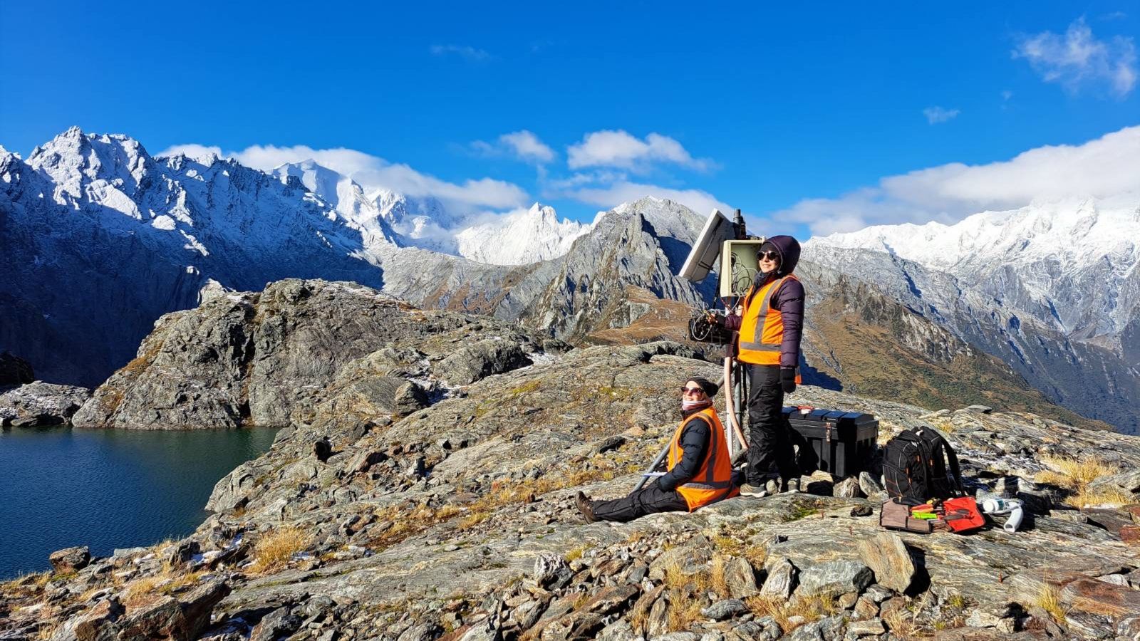 Two students pose on the Southern Alps by a seismometer 