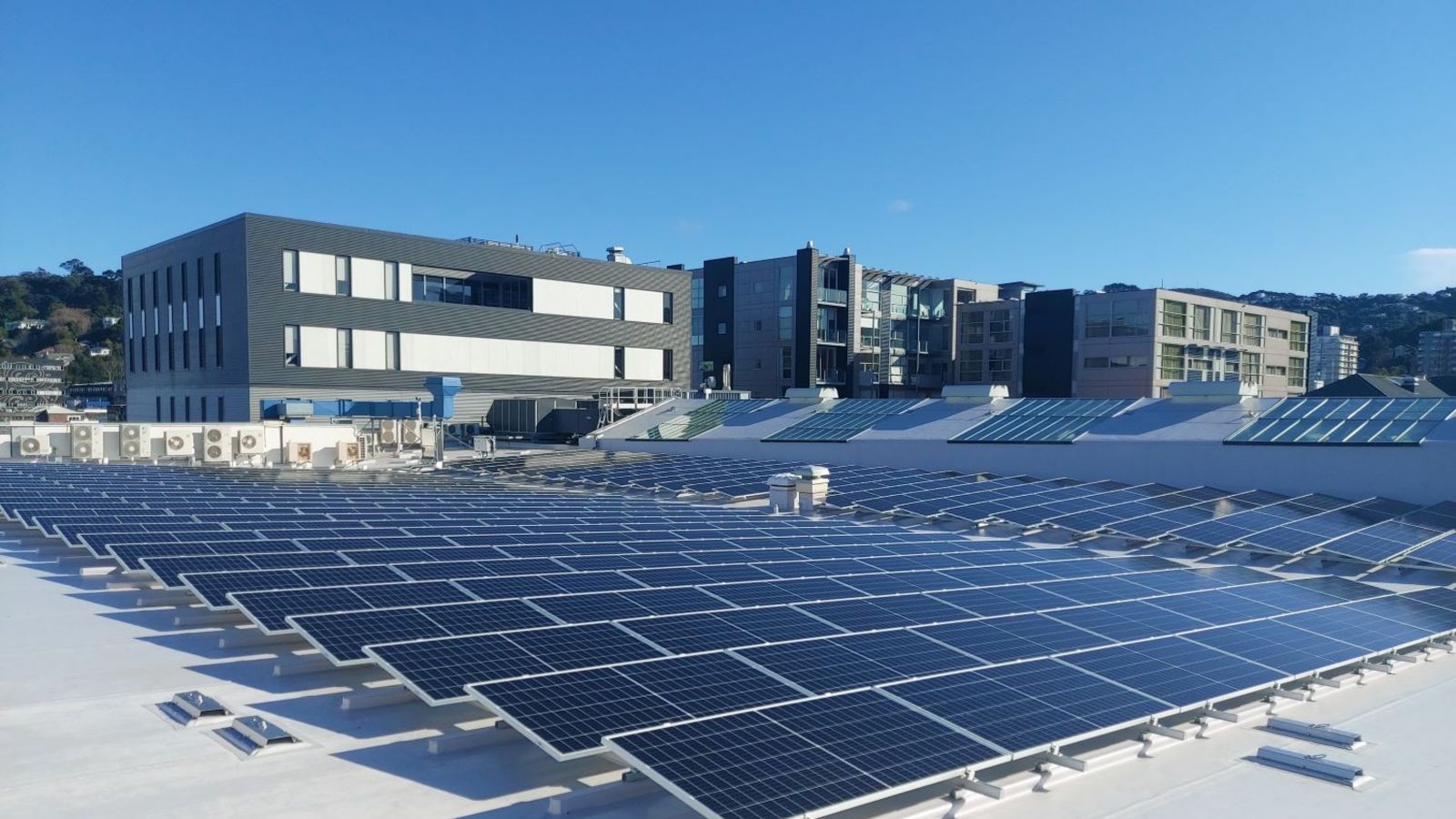 An array of solar panels on top of a city building against the blue sky. 