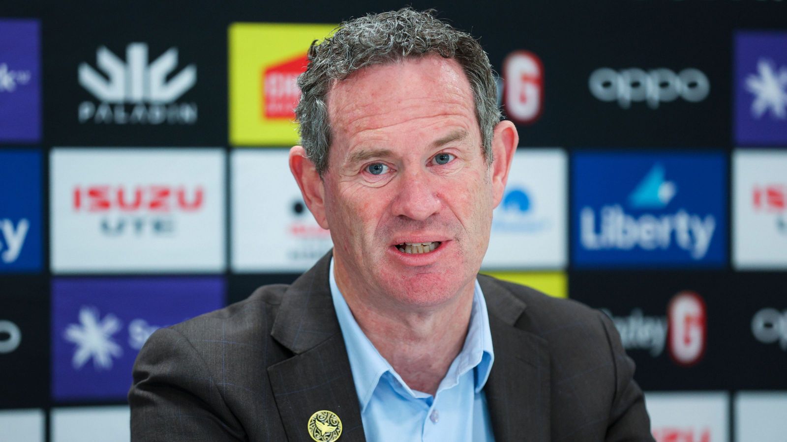 Man wearing suit looking at camera against background with sponsors logos. Phoenix pin on blazer. 