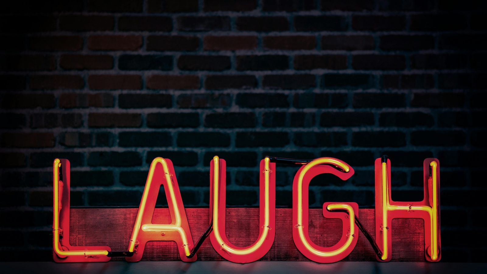 Neon 'laugh' sign against a dark wall 