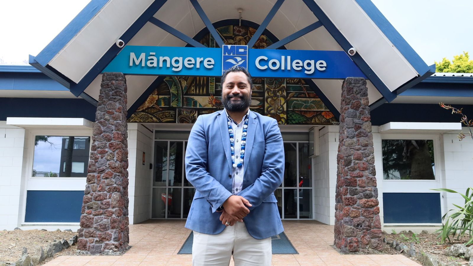 Pasifika man wearing a lei and smiling in front of Mangere College