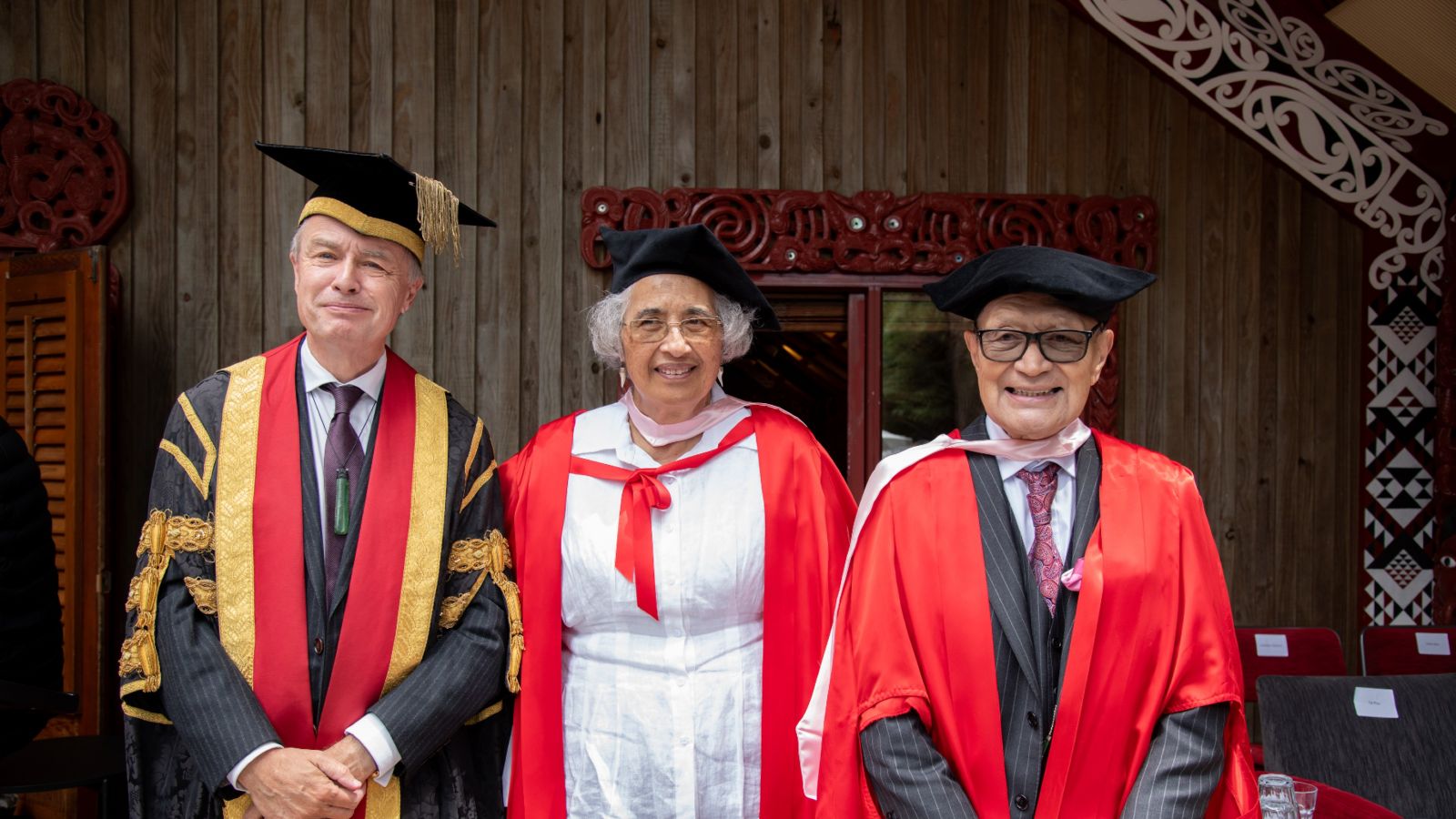 Chancellor John Allen with the two Honorary Doctorate recipients, standing in front of Te Herenga Waka's marae