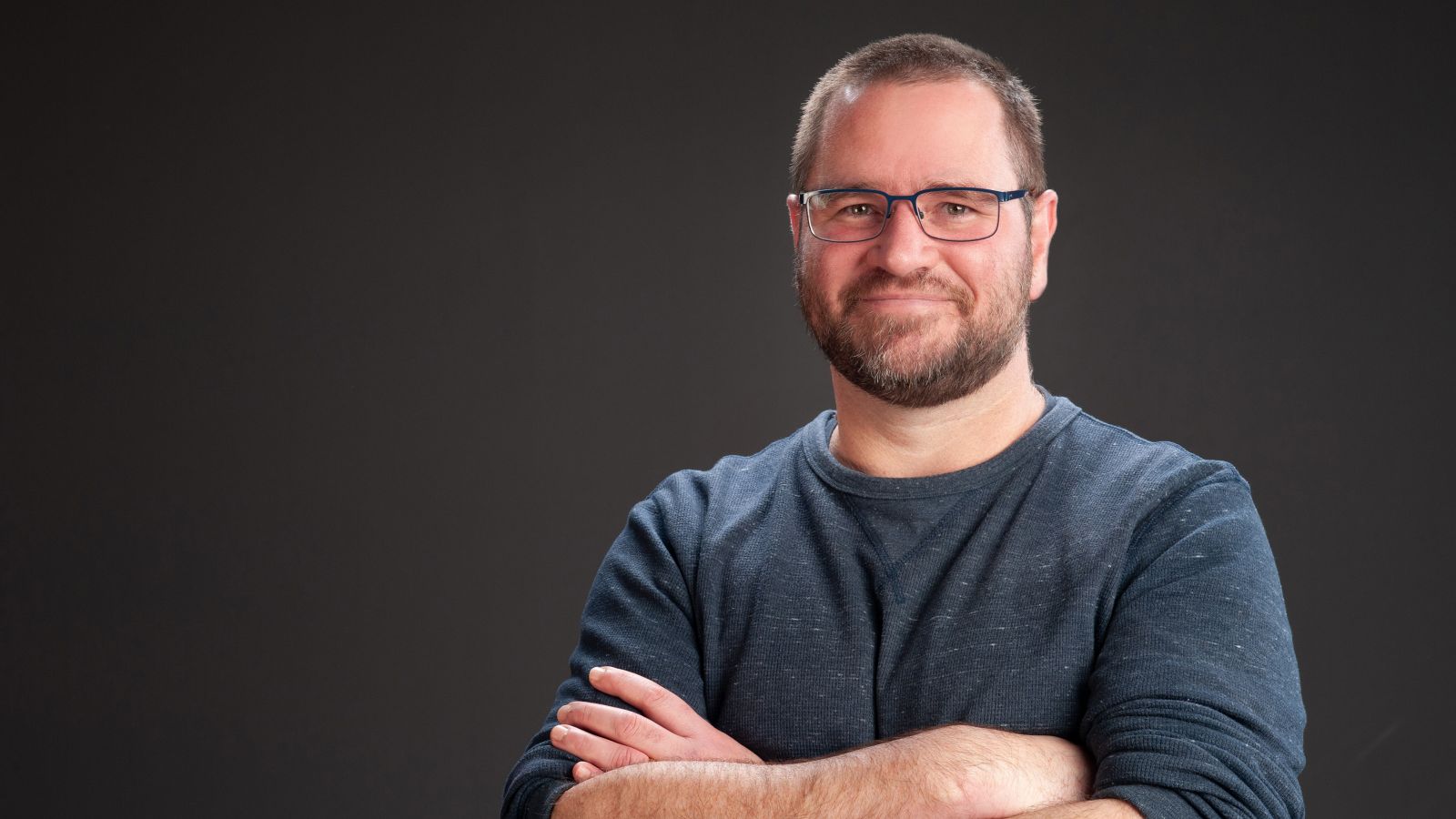 A smiling man with folded arms, short hair and glasses