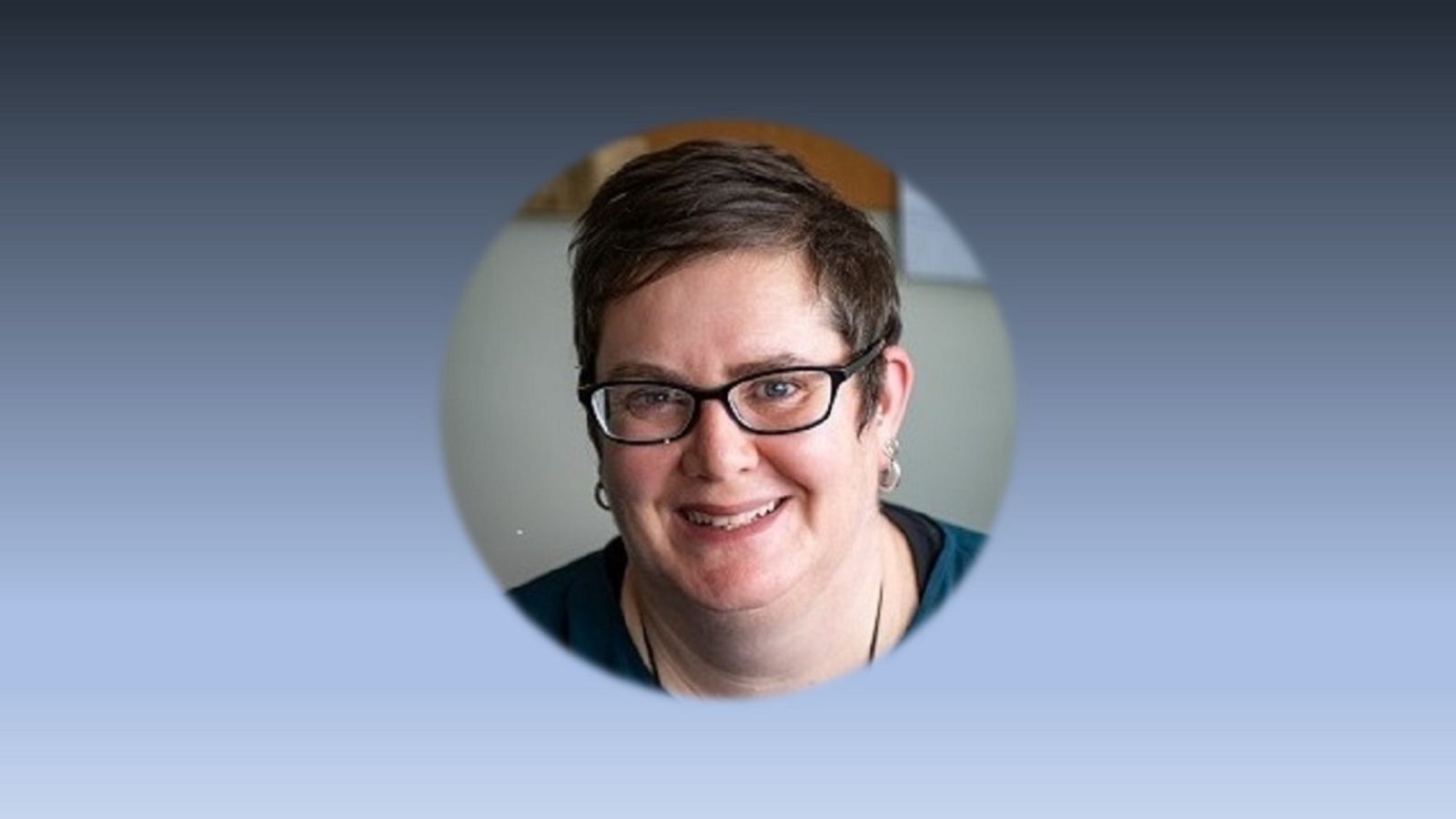 A woman with short hair and glasses smiles at the camera