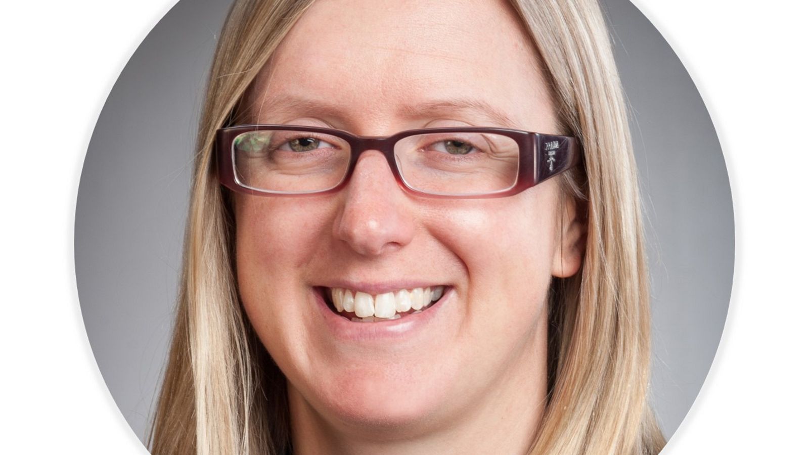 A woman with blonde hair and glasses smiles at the camera