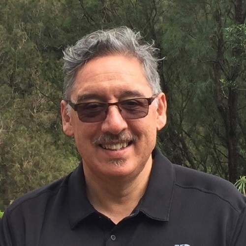A man with grey hair and glasses wearing a black shirt smiles at the camera